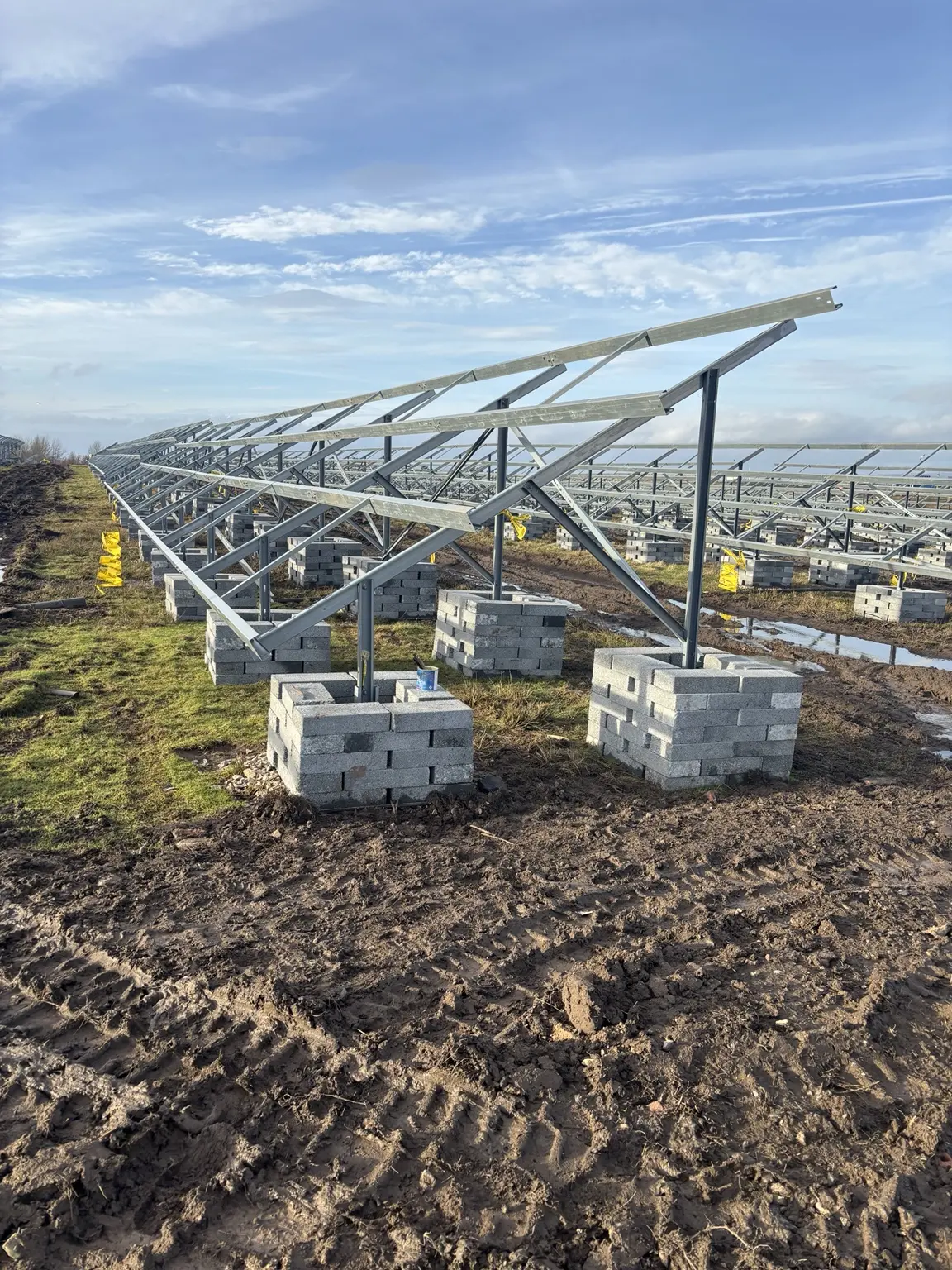 Ground-mount solar frames installed across a muddy field with temporary block support