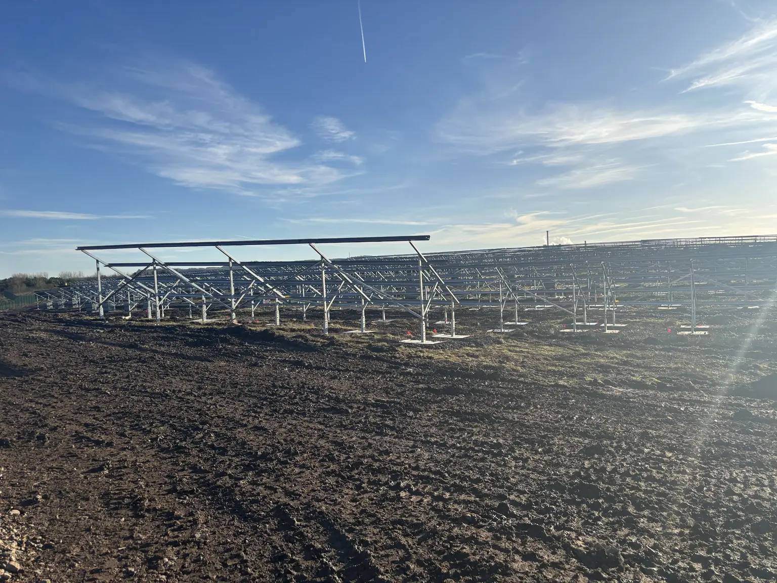 Ground-mount solar farm under construction with extensive galvanized racking across a muddy UK site